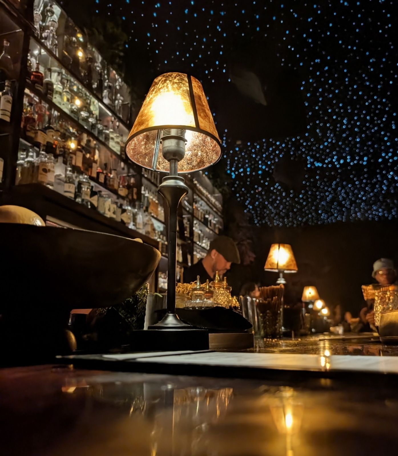 Selva — view from a seat at the bar, lamp glow over marble, fiber-optic ceiling above